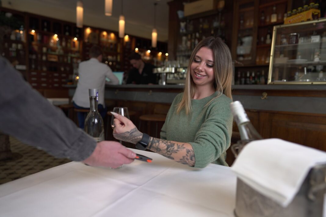 Kobieta płaci zegarkiem przy restauracyjnym stole Kobieta płaci zegarkiem przy restauracyjnym stole